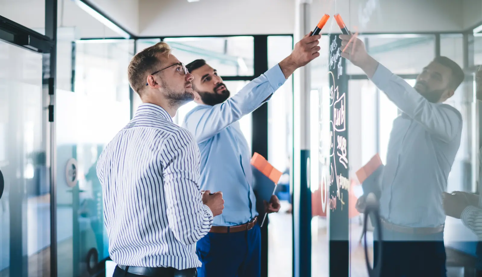 Two men discussing content on a whiteboard in a business setting. Two men discussing content on a whiteboard in a business setting.