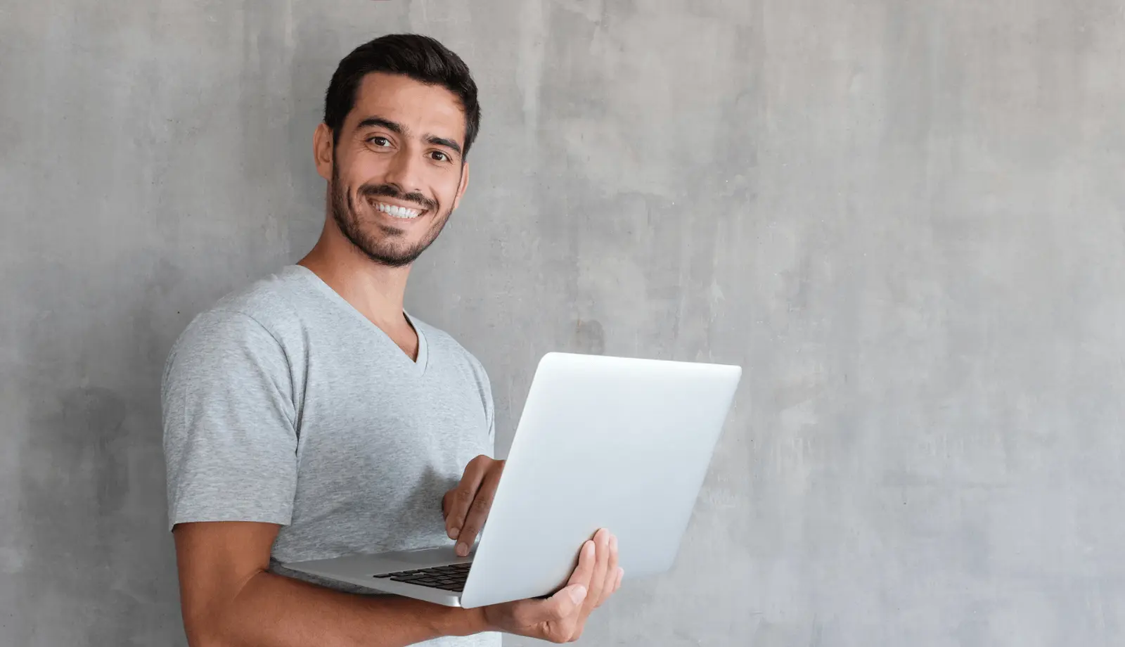young man smiling at the camera and holding a laptop young man smiling at the camera and holding a laptop