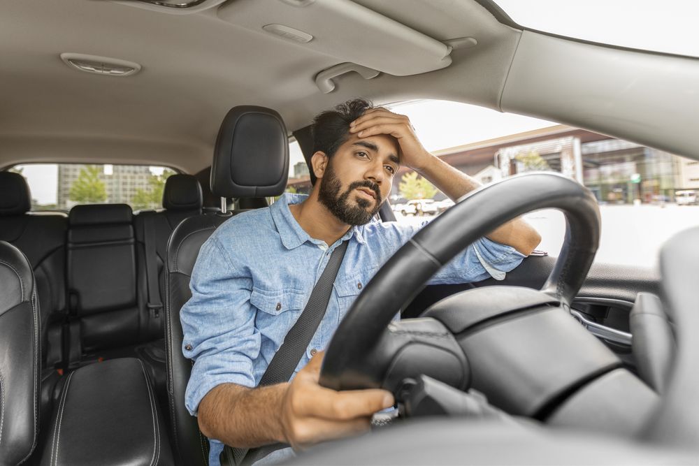 Mann sitzt am Steuer und hält genervt Hand an Stirn.