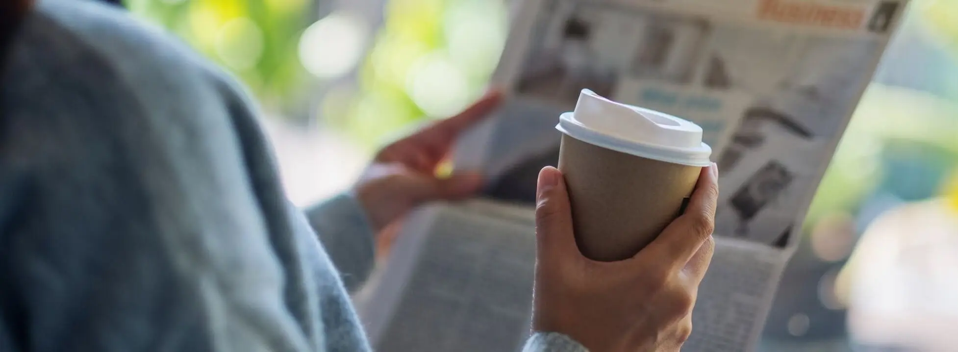 Kobieta trzymająca kubek z kawą, przeglądająca gazetę z aktualnymi wiadomościami Kobieta trzymająca kubek z kawą, przeglądająca gazetę z aktualnymi wiadomościami