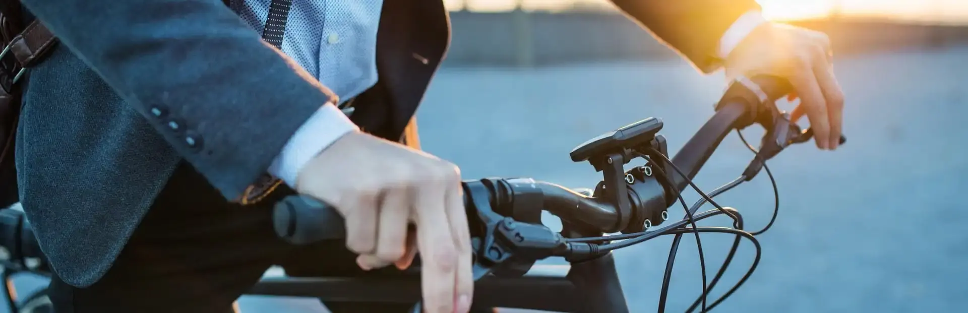 Zbliżenie na dłonie mężczyzny jadącego na rowerze elektrycznym, na tle zachodzącego słońca Zbliżenie na dłonie mężczyzny jadącego na rowerze elektrycznym, na tle zachodzącego słońca