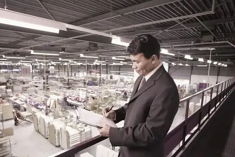 Mężczyzna w garniturze, znajdujący się na produkcji, pisze na kartce papieru, symbolizując badanie bezpieczeństwa produktów