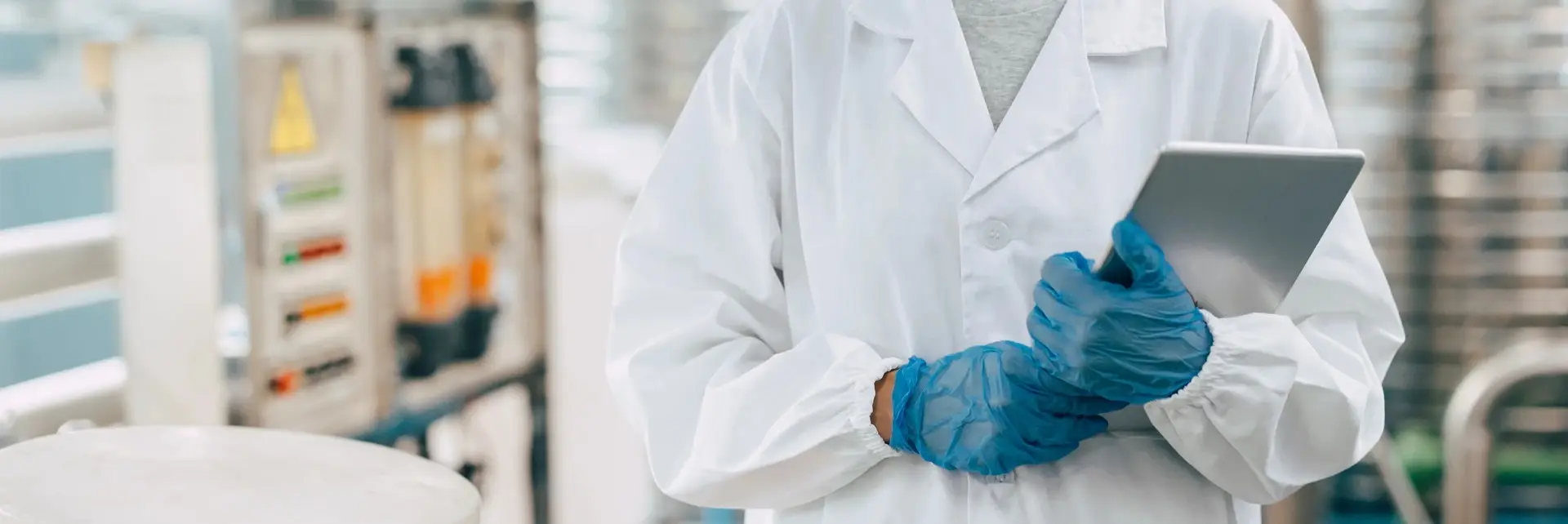 Pracownik w odzieży ochronnej i rękawiczkach wykonujący kontrolę jakości żywności z tabletem w zakładzie produkcyjnym. Pracownik w odzieży ochronnej i rękawiczkach wykonujący kontrolę jakości żywności z tabletem w zakładzie produkcyjnym.