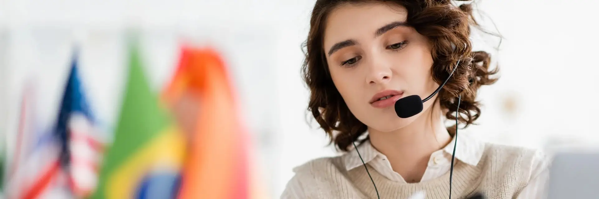 Tłumacz ze słuchawkami i mikrofonem w pracy, na tle flag różnych państw, symbolizujący certyfikację ISO 17100 