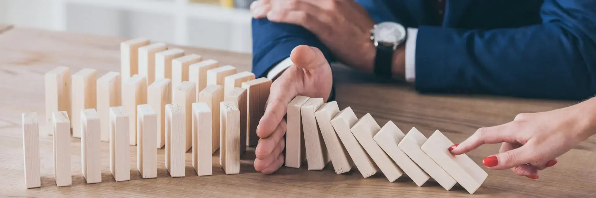 Palec kobiety pchający drewniany element oraz menedżer zatrzymujący efekt domina, symboliczne ujęcie certyfikacji ISO 22301