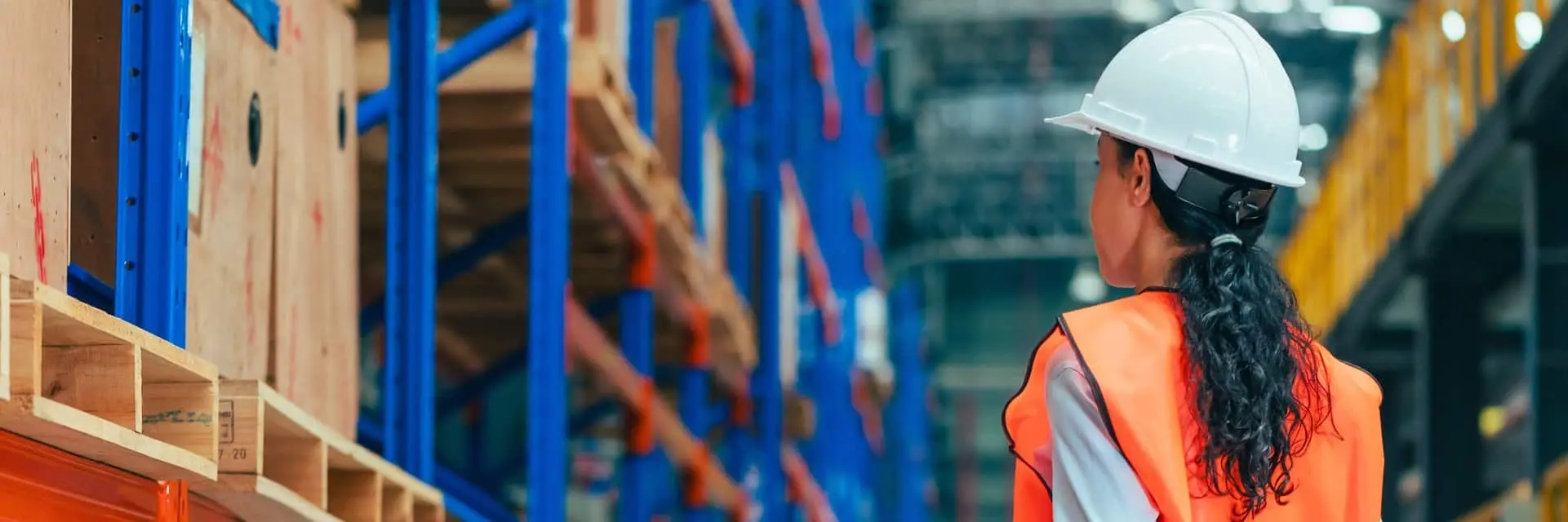 Kobieta w kamizelce odblaskowej i kasku rozgląda się po magazynie, symbolizując certyfikację ISO 45001 Kobieta w kamizelce odblaskowej i kasku rozgląda się po magazynie, symbolizując certyfikację ISO 45001