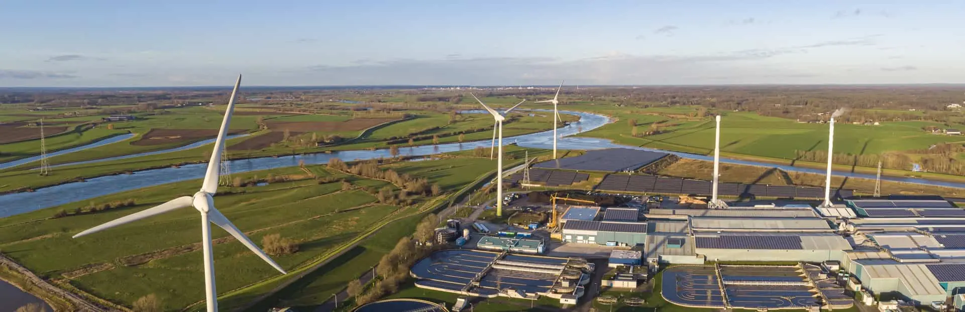 Turbiny wiatrowe w płaskim, nadrzecznym krajobrazie, symbolizujące certyfikację ISO 50001 Turbiny wiatrowe w płaskim, nadrzecznym krajobrazie, symbolizujące certyfikację ISO 50001