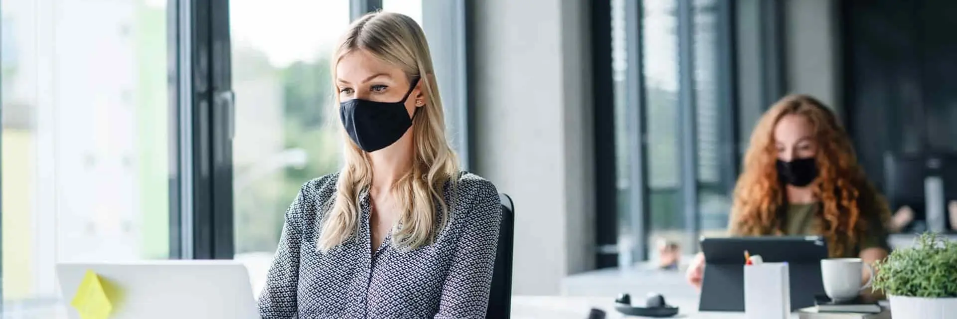 Kobiety pracujące w biurze na laptopach, w maseczkach na twarzy, symbolizujące certyfikację ISO/PAS 45005
