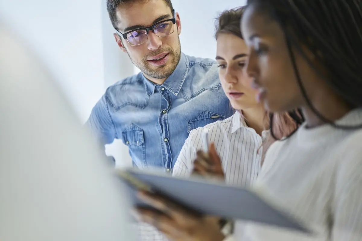 Trzy osoby dyskutujące nad dokumentem w procesie certyfikacji osób Trzy osoby dyskutujące nad dokumentem w procesie certyfikacji osób