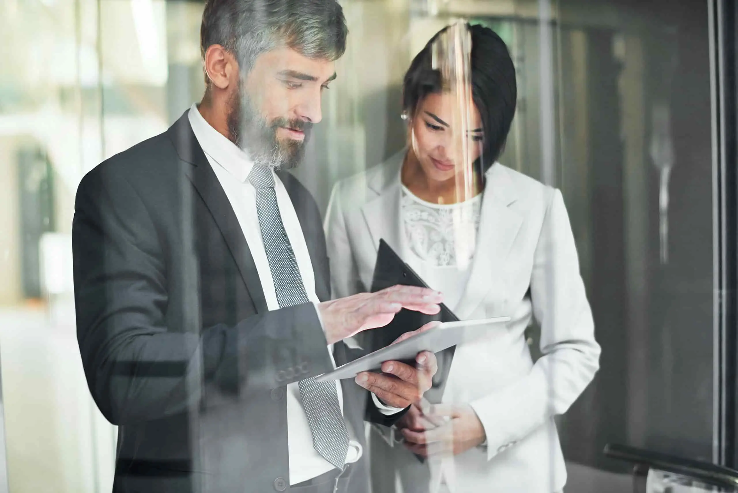 Dwoje pracowników w formalnym stroju przeglądających dokumenty na tablecie, symbolizujących certyfikację systemów zarządzania