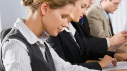 Grupa osób siedzących przy stole i zapisujących notatki podczas szkolenia lub spotkania