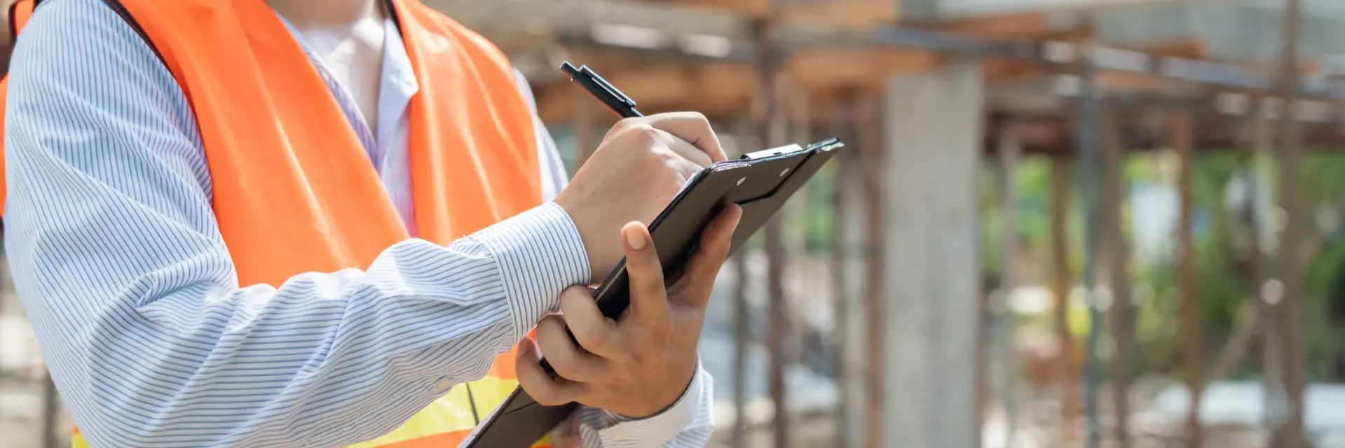 Pracownik w kamizelce odblaskowej wypełniający dokumenty na clipboardzie, symbolizujący bezpieczeństwo w pracy Pracownik w kamizelce odblaskowej wypełniający dokumenty na clipboardzie, symbolizujący bezpieczeństwo w pracy