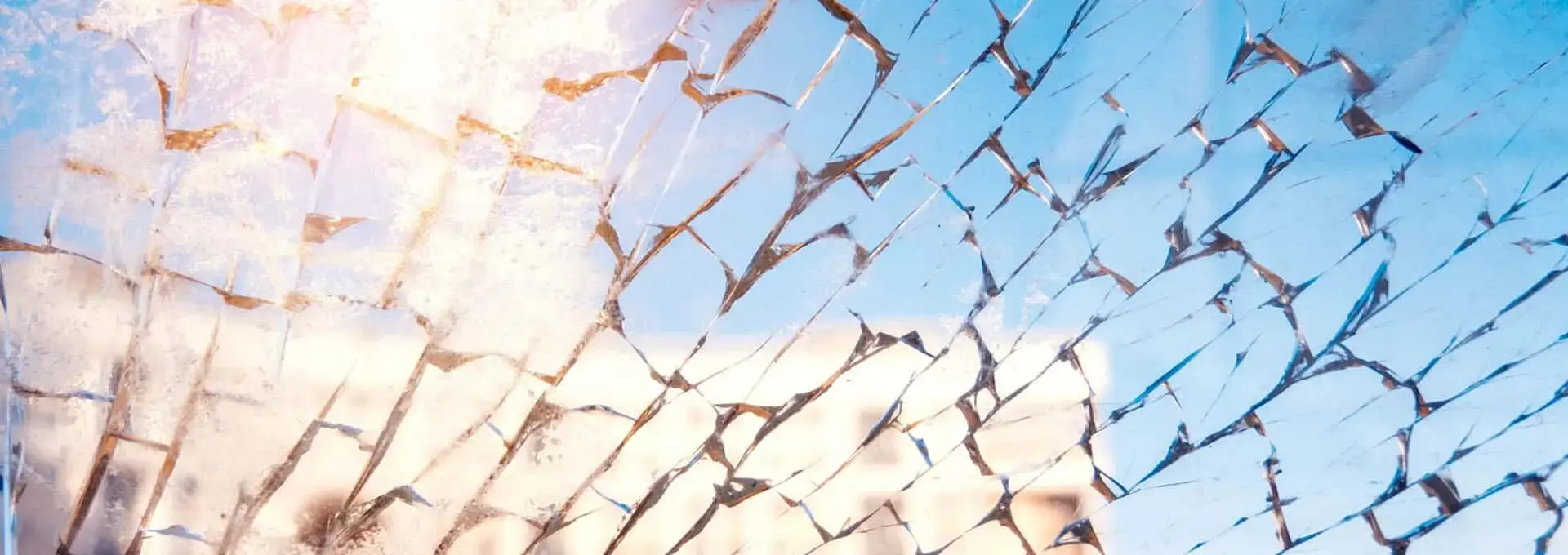 Rozbite okno na tle miasta, na które pada światło słoneczne, symbolizujące weryfikację zarządzania jakością producentów stłuczki szklanej