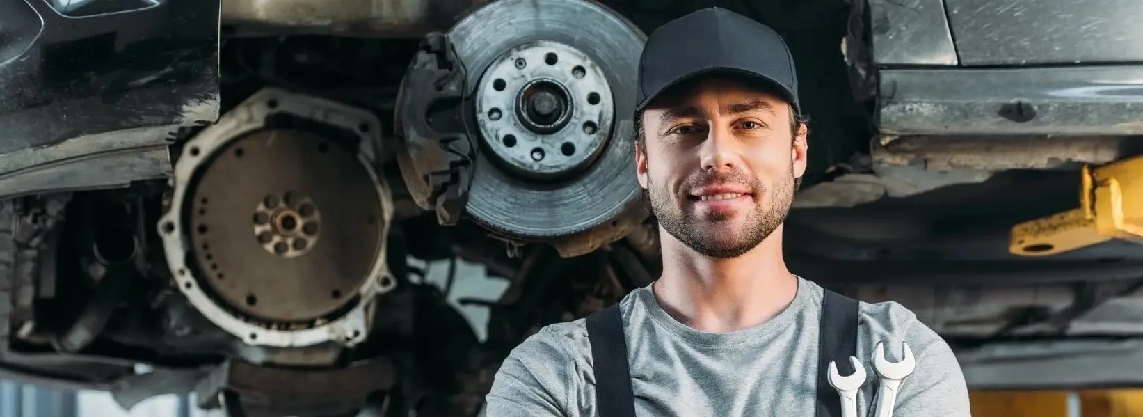 Pracownik warsztatu samochodowego z autem w tle, symbolizujący certyfikację SERMI Pracownik warsztatu samochodowego z autem w tle, symbolizujący certyfikację SERMI