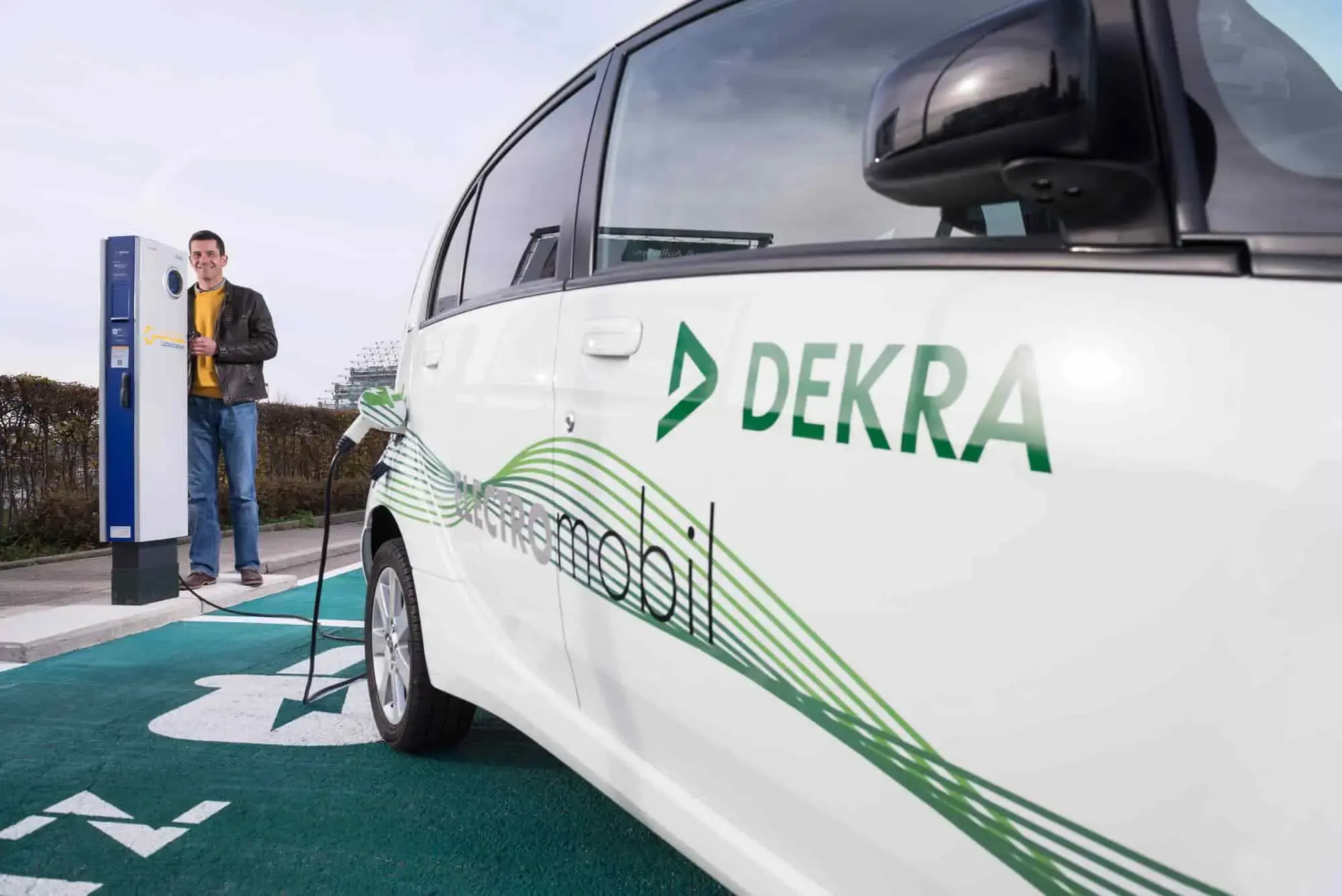 Samochód elektryczny DEKRA na stacji ładowania, przedstawiający testy pojazdów elektrycznych i infrastruktury ładowania