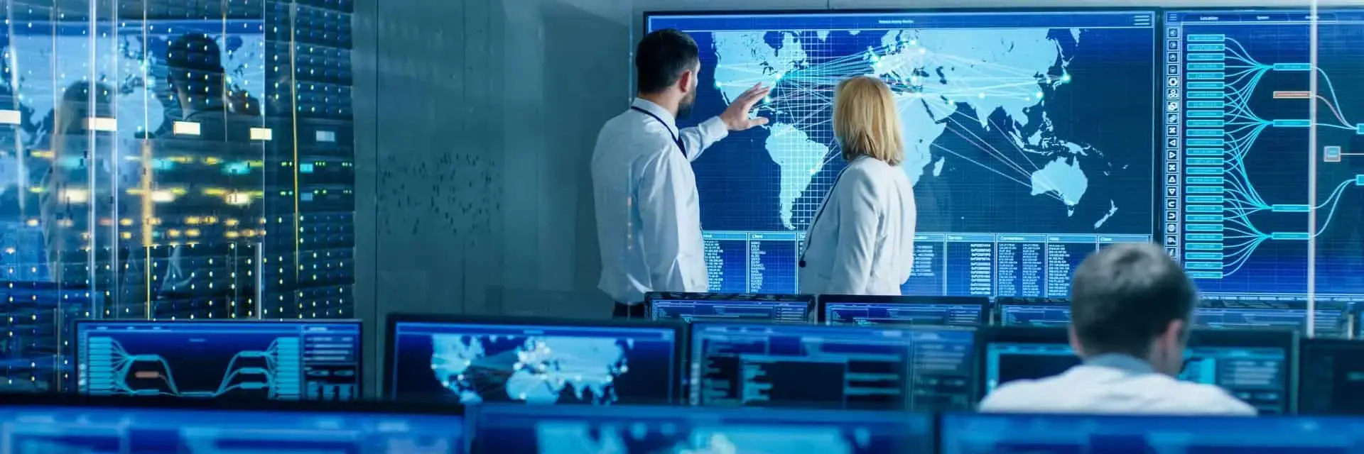 Kobieta i mężczyzna znajdujący się w centrum danych przed dużym ekranem z interaktywną mapą, rozmawiający o cyberbezpieczeństwie Kobieta i mężczyzna znajdujący się w centrum danych przed dużym ekranem z interaktywną mapą, rozmawiający o cyberbezpieczeństwie