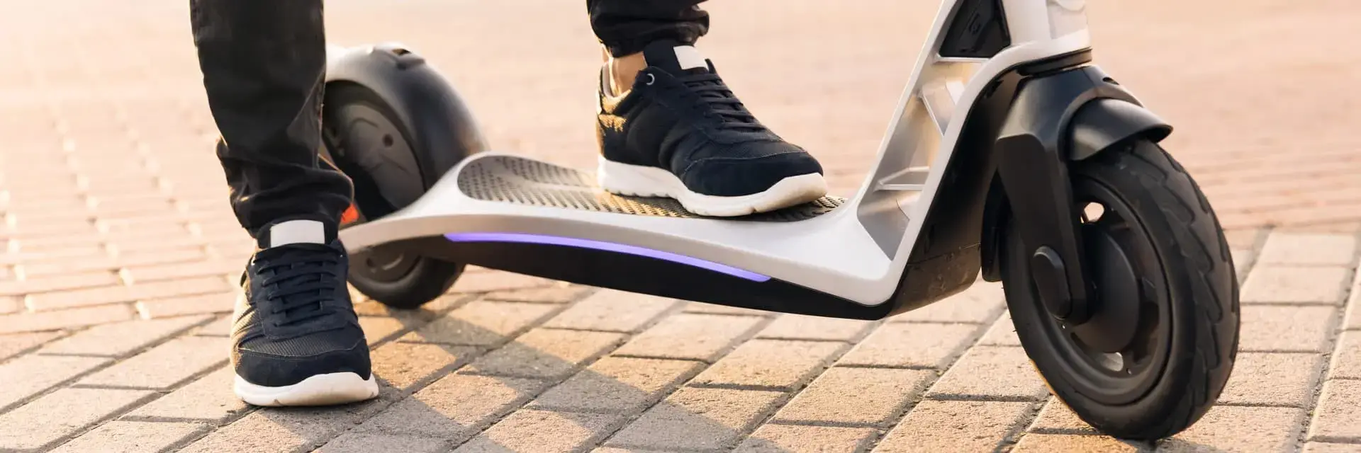 Mężczyzna z jedną stopą na hulajnodze elektrycznej zaparkowanej na chodniku Mężczyzna z jedną stopą na hulajnodze elektrycznej zaparkowanej na chodniku