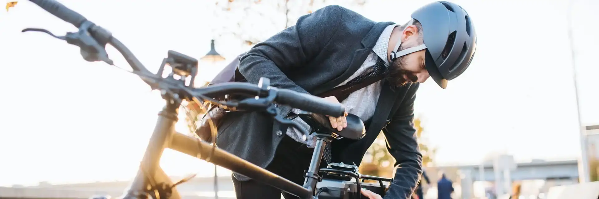 Mężczyzna w kasku przygląda się swojemu rowerowi elektrycznemu stojącemu w parku Mężczyzna w kasku przygląda się swojemu rowerowi elektrycznemu stojącemu w parku