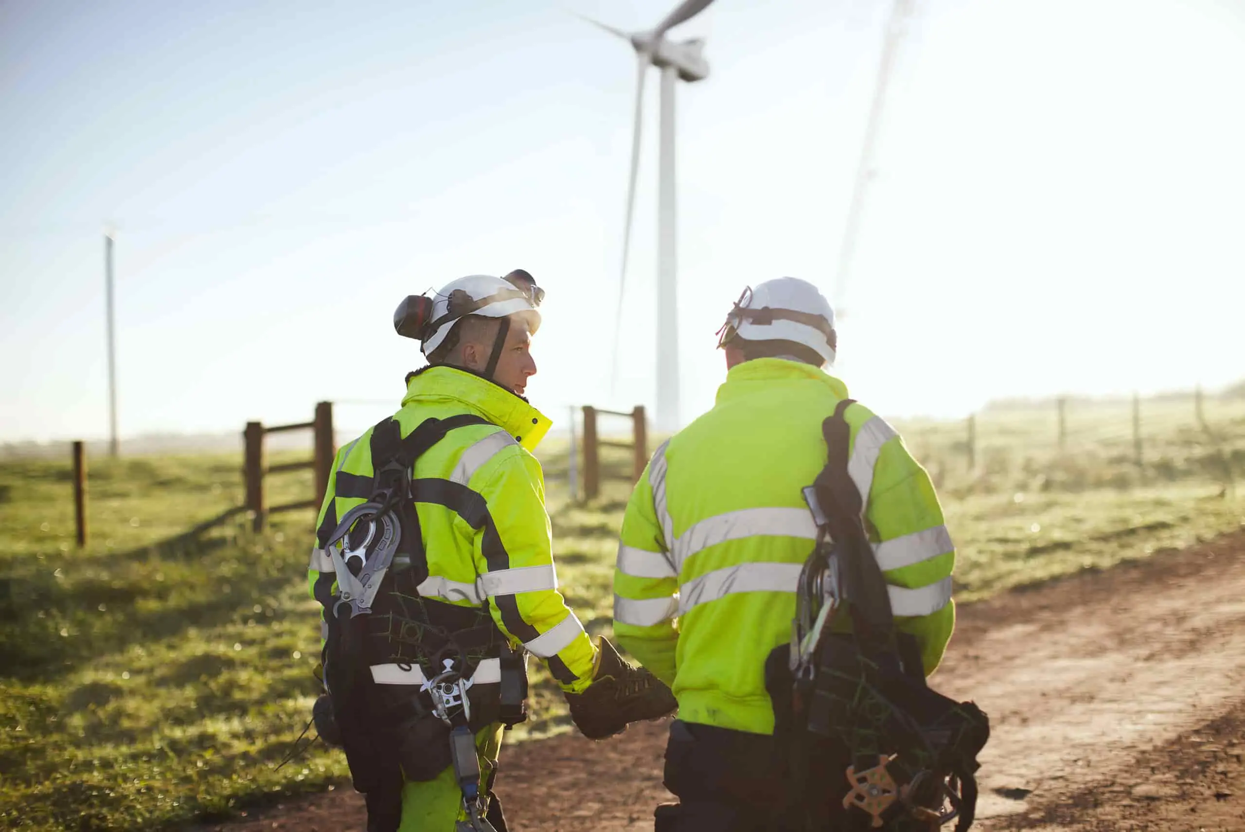 Pracownicy w kamizelkach ochronnych przy turbinie wiatrowej, symbolizujący zarządzanie bezpieczeństwem zdrowia i środowiskiem