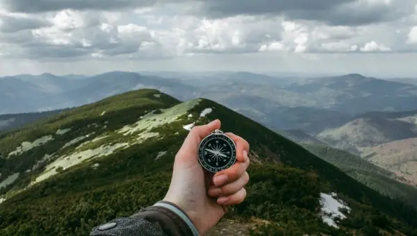 Ręka trzymająca kompas na tle górskiego krajobrazu – zarządzanie i ład korporacyjny DEKRA, zrównoważony rozwój i odpowiedzialność