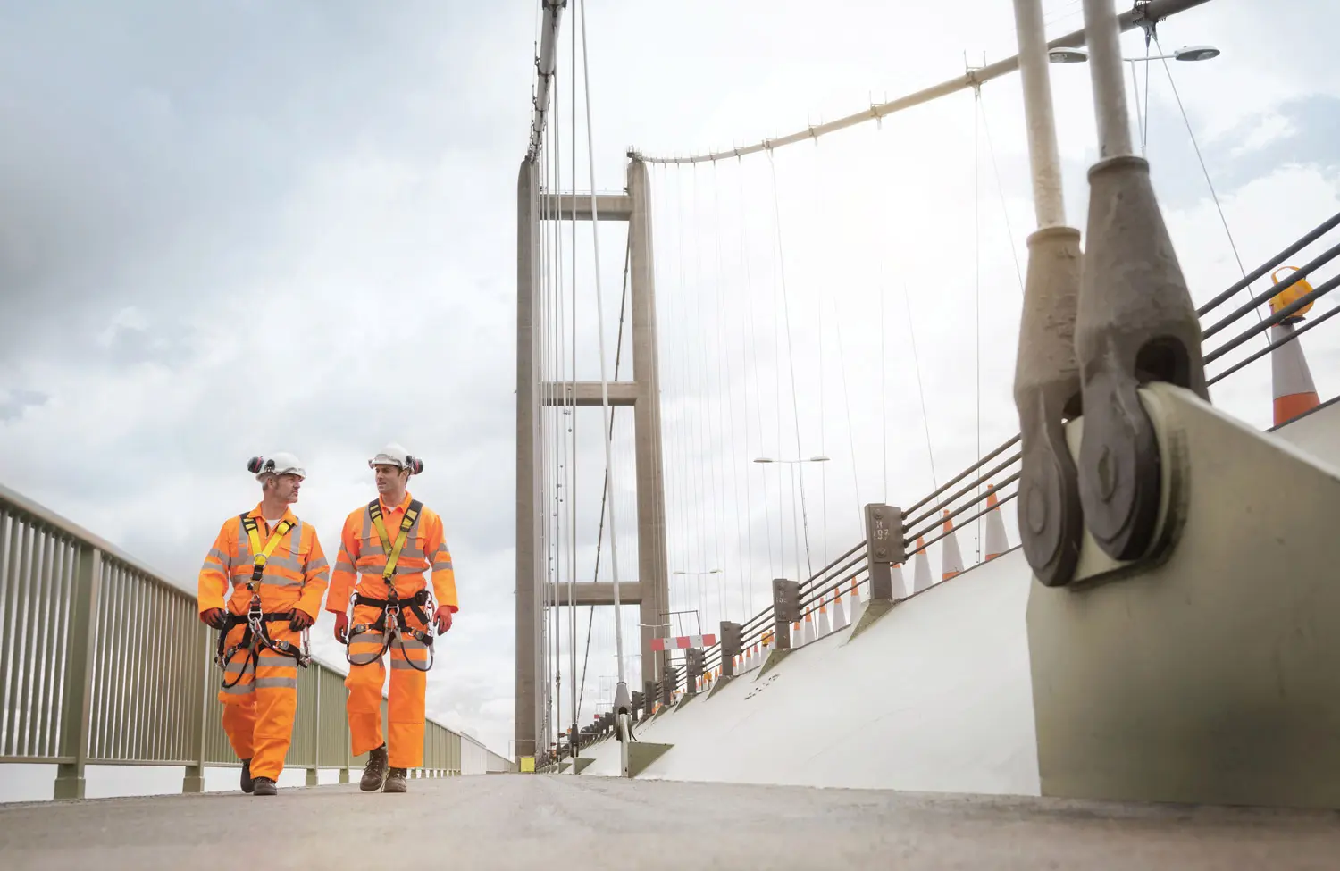 Zwei Arbeiter in Schutzkleidung laufen über eine Brücke 