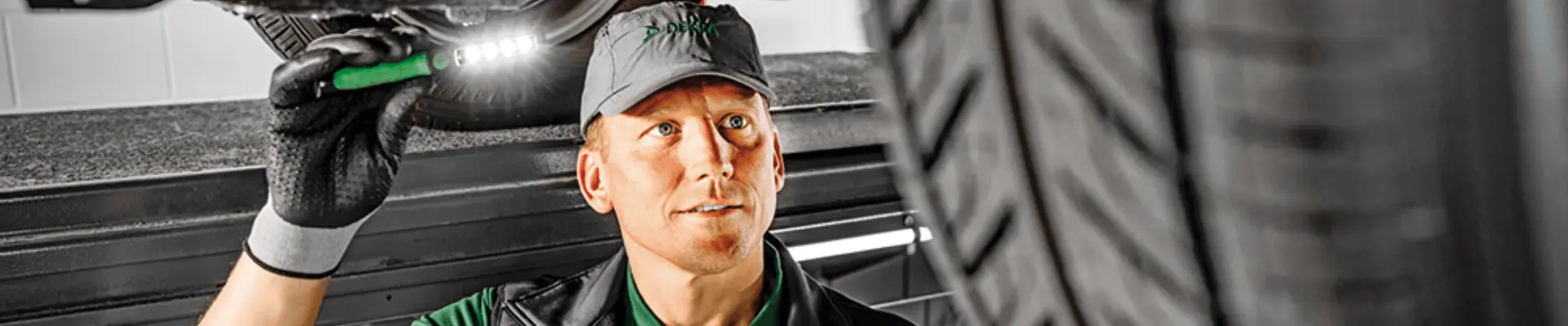 DEKRA-katsastaja käyttää taskulamppua tutkiessaan tarkasti ajoneuvon alustaa katsastuksen aikana, varmistaen turvallisuuden ja vaatimustenmukaisuuden.