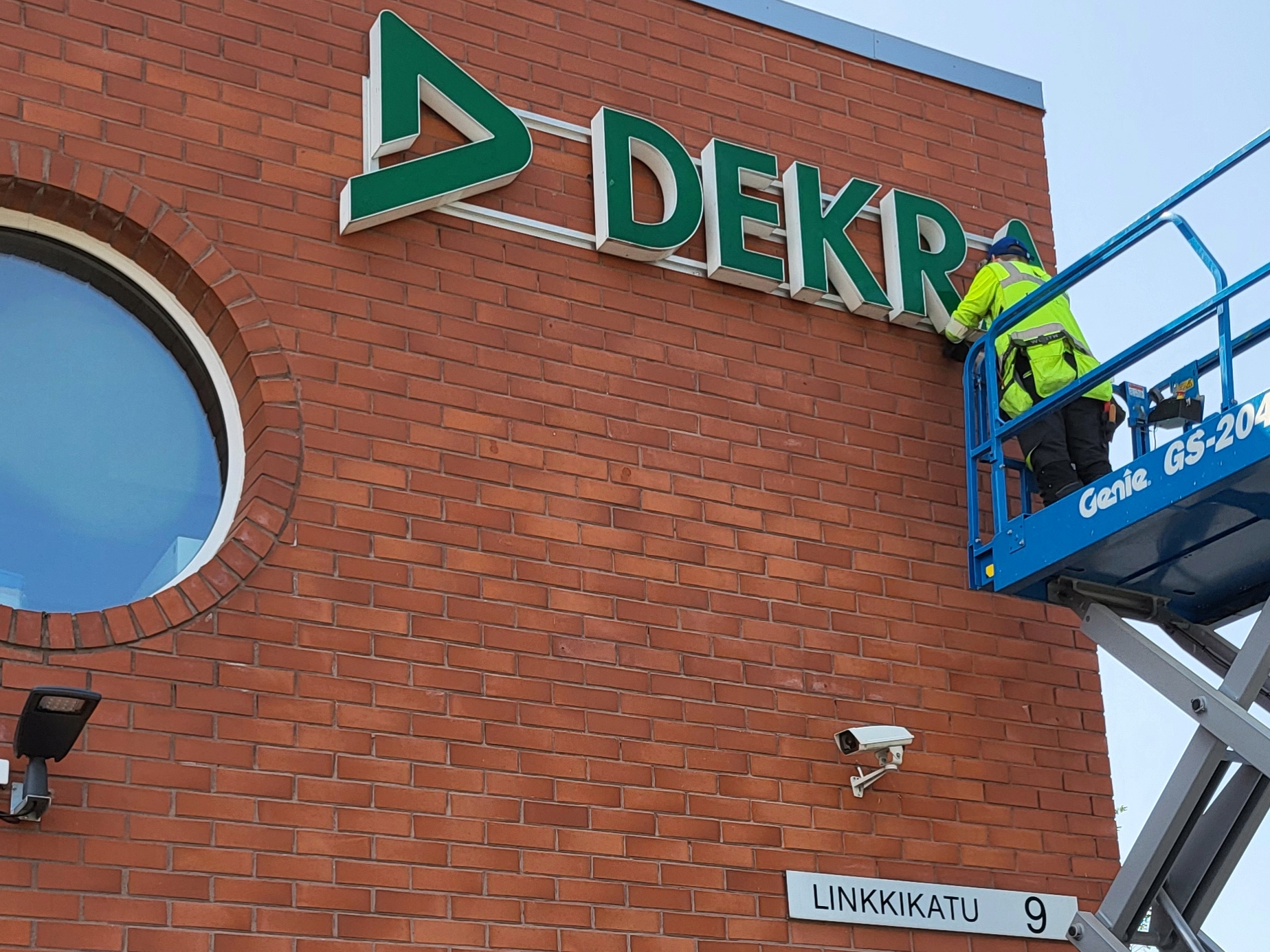 Punatiiliseinään kiinnitetään DEKRA valomainoskylttiä osoitteessa Linkkikatu 9. 