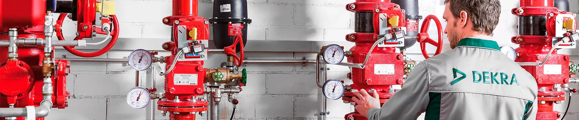 DEKRAn asiantuntija tarkastamassa punaisia seinään kiinnitettyjä sammutuslaitteistoja