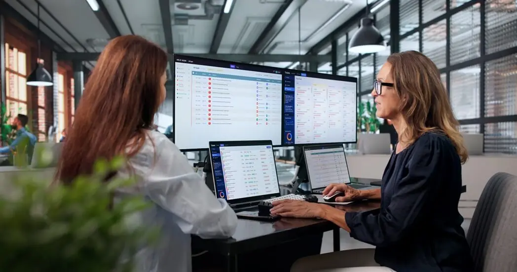 Two people sitting in front of several computer screens. Two people sitting in front of several computer screens.