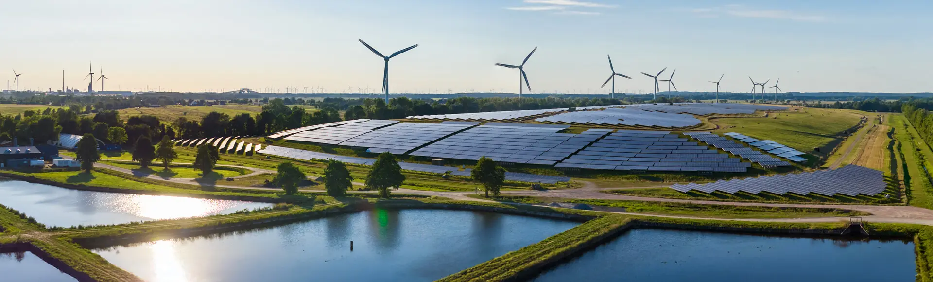 Åkrar av gräs med flera vindkraftverk längs horisonten och solpaneler längs marken.