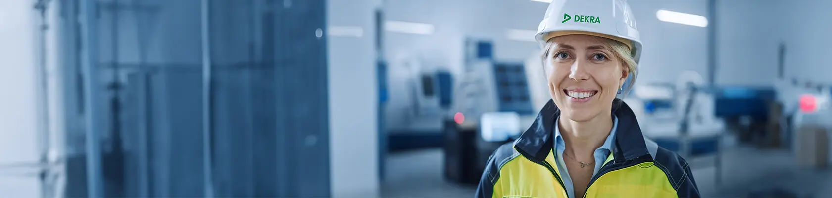 En kvinna som befinner sig i en industriell arbetsplats iförd en vit hjälm och en gul jacka