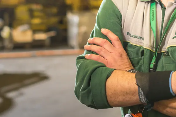 A man wearing a green and white overalls standing in an industrial setting showing off his work environment.