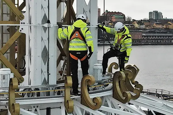 Two surveying engineers stand high up in a funfair ride, with a vibrant city skyline visible in the background.