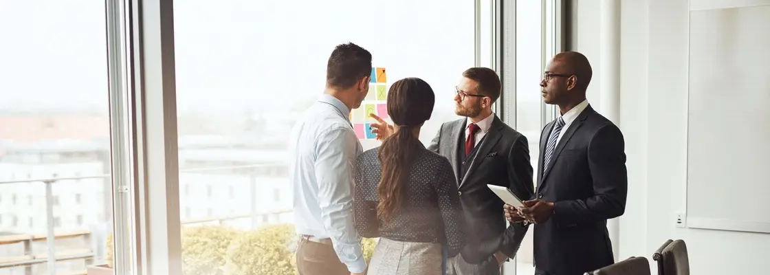 Four people standing in front of a large window in a conference room and talking.