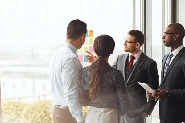 Four people standing in front of a large window in a conference room and talking.