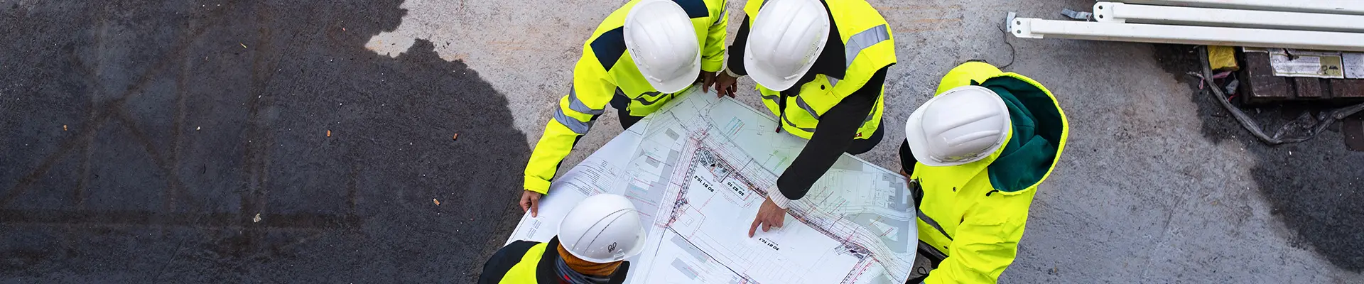  En mångfaldig grupp individer som bär ljusgula västar står tillsammans, engagerade i en konstruktionsritning.