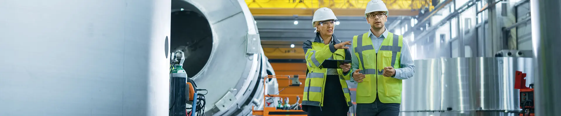 A man and a woman wearing reflective vests walk and check the building in an industrial setting