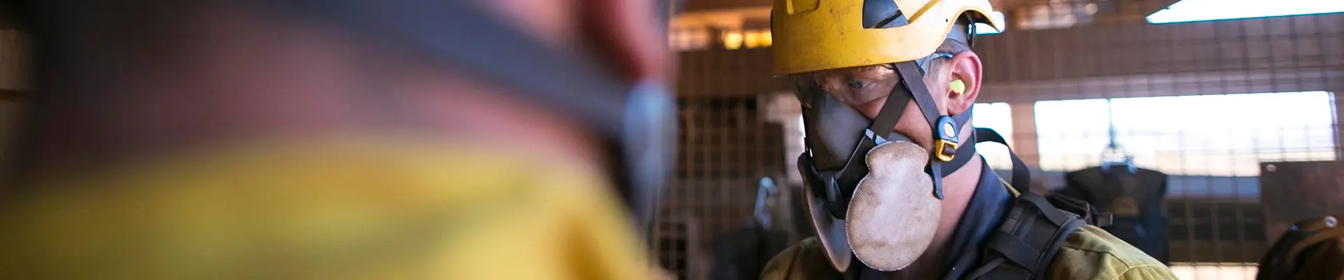  En man i hjälm och gul jacka står självsäkert, redo för arbete i byggmiljö.