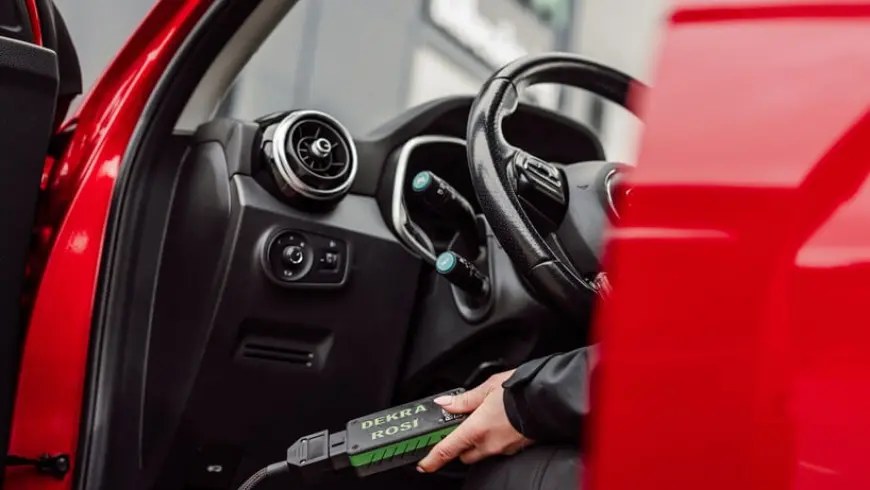 A person in black clothes sitting in the driver's seat holding an iPad and a box of battery tests.