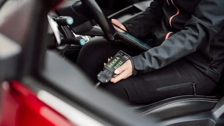 A person in black clothes sitting in the driver's seat holding an iPad and a box of battery tests.