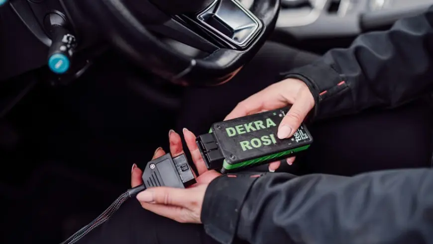 A person in black clothes sitting in the driver's seat holding an iPad and a box of battery tests.