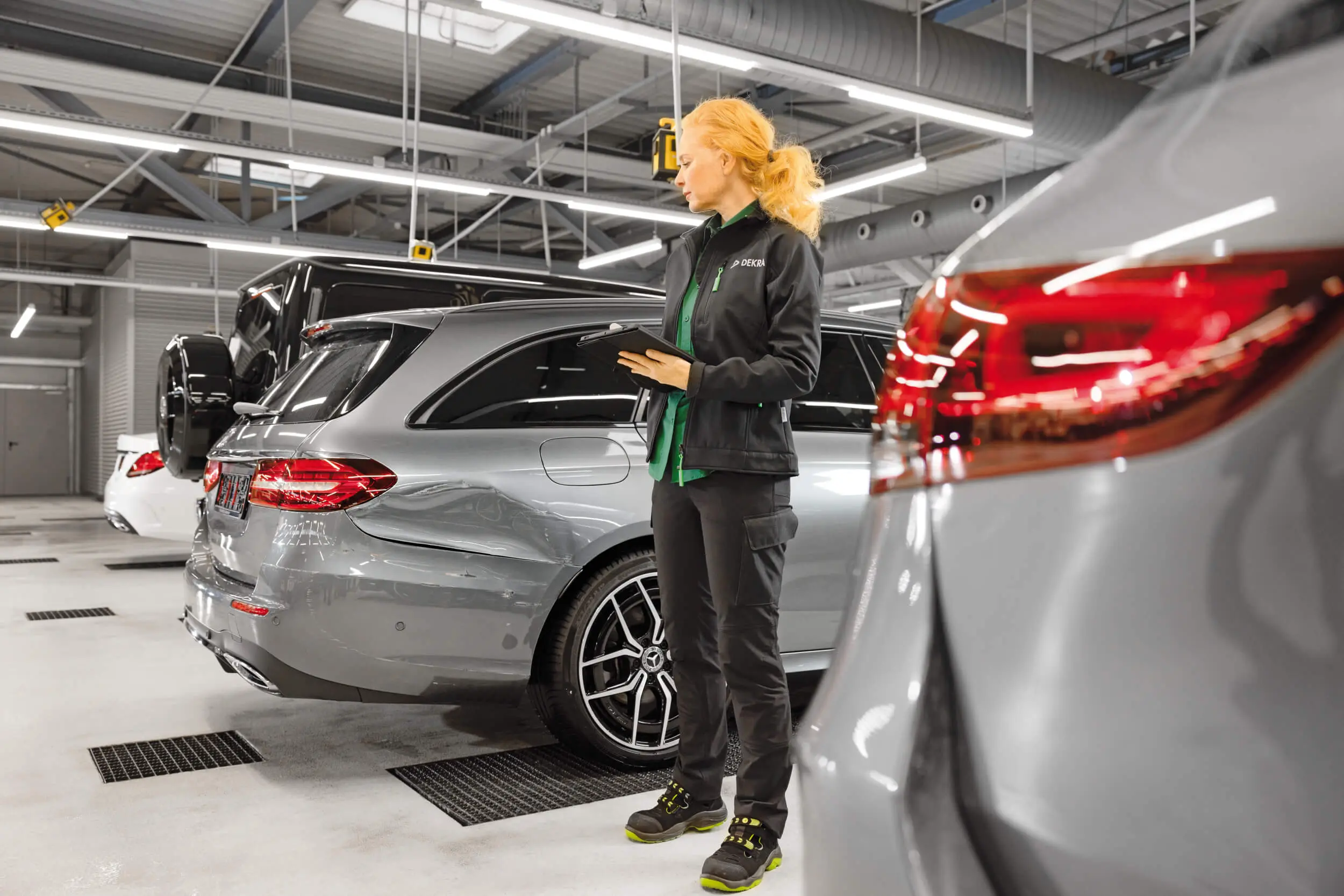 A woman in black work clothes standing in a garage holding an iPad.