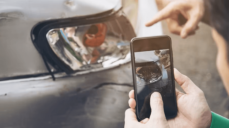 Bild på en mobiltelefon med kamera som en person riktar mot en bilskada. 