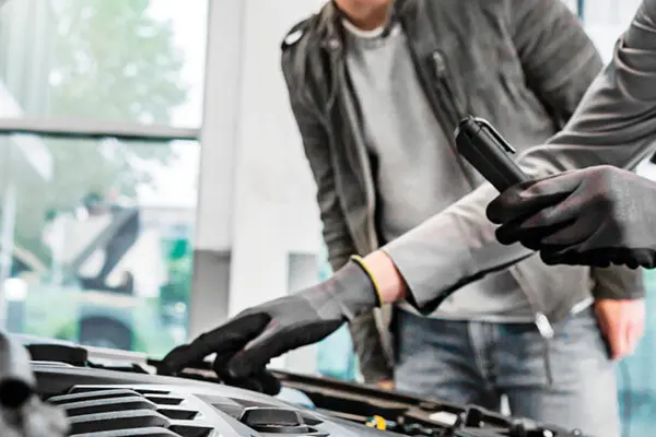 A person is leaning over a car engine with the hood open and looking at the engine.