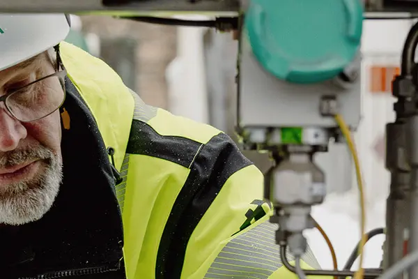 A man in reflective clothing and a white helmet inspecting cables. A man in reflective clothing and a white helmet inspecting cables.