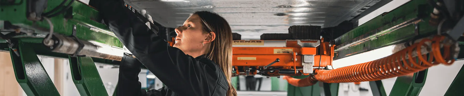 A woman carrying out a car inspection stands under a car that is raised, she inspects the car from below and shines a flashlight. A woman carrying out a car inspection stands under a car that is raised, she inspects the car from below and shines a flashlight.