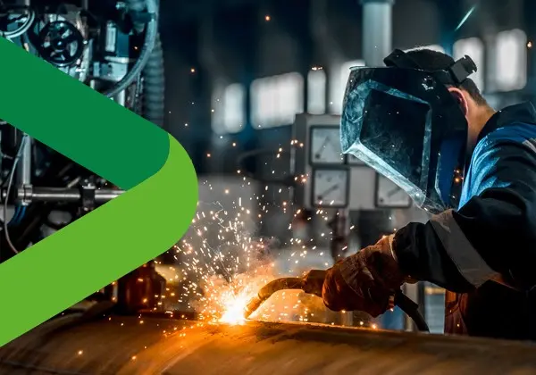 En svetsare med skyddshjälm som lutar sig fram över ett objekt med svetsen och det flyger gnistor.