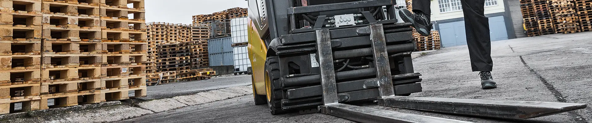  En gaffeltruck parkerad bredvid en hög trave med träpallar i lagermiljö, som visar upp industriell utrustning och förvaring.