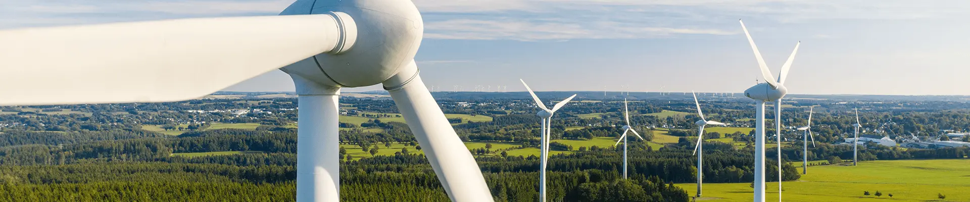 En vindturbin på ett vindkraftverk med åkrar och himmel i bakgrunden.