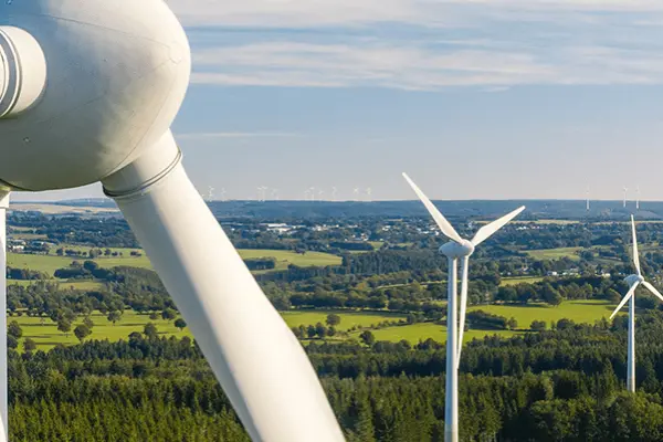 A wind turbine on a wind farm with fields and sky in the background.